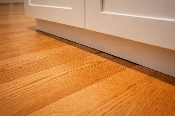 Hardwood floor installed before cabinets showing expansion gap at kitchen cabinet base